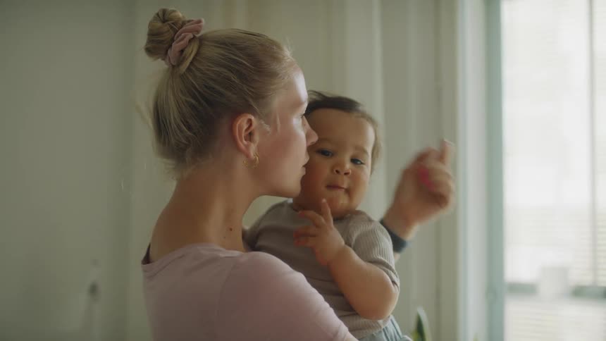 A woman kisses a baby on the cheek while carrying it in her arms