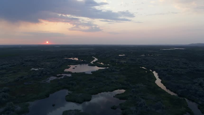 Small lakes and streams cover a natural wetlands area as the rising sun glows red on the horizon