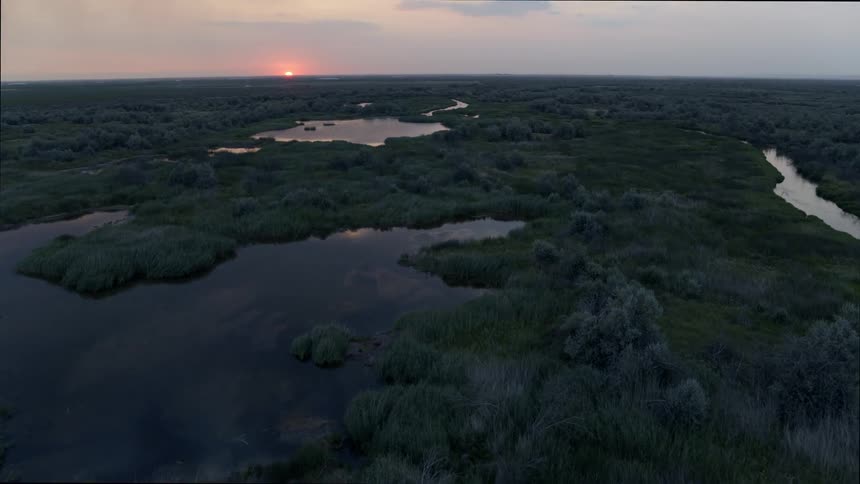 Small lakes and wetlands are surrounded by native vegetation and a natural landscape as the sun sits just above the horizon