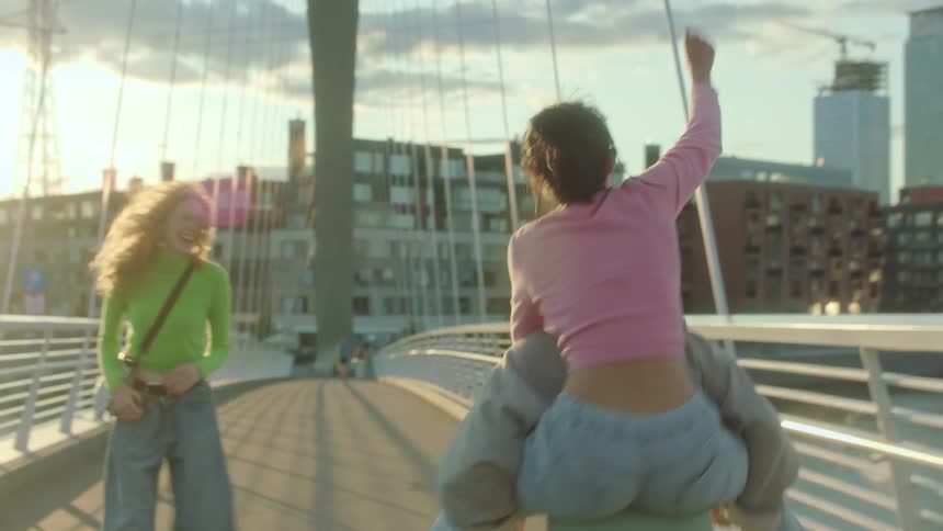 Three teenage girls horsing around and laughing while crossing a city bridge