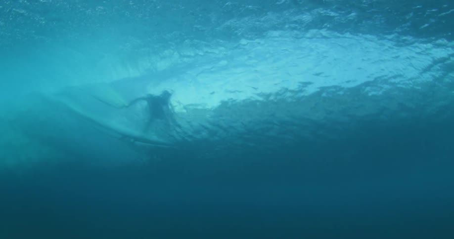 Looking up from under the water a surfer can be seen riding a wave