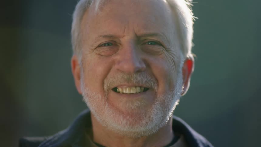 An elderly man with a gray beard smiling for a portrait