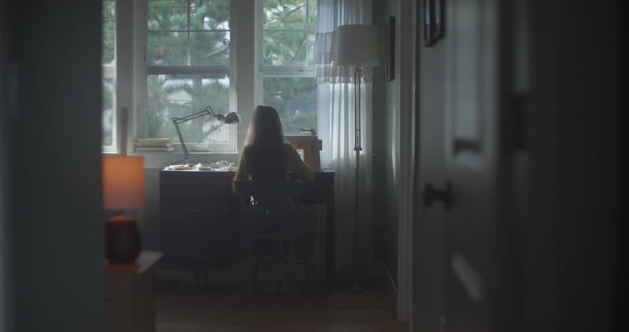 A woman is working at a desk facing a window inside her home