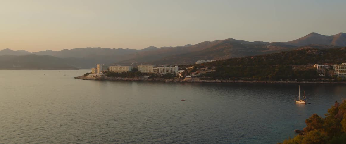A lake with a boat with buildings a mountain range sky and clouds in the background