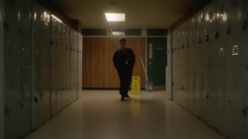 A man puts a wet floor sign in a school hallway