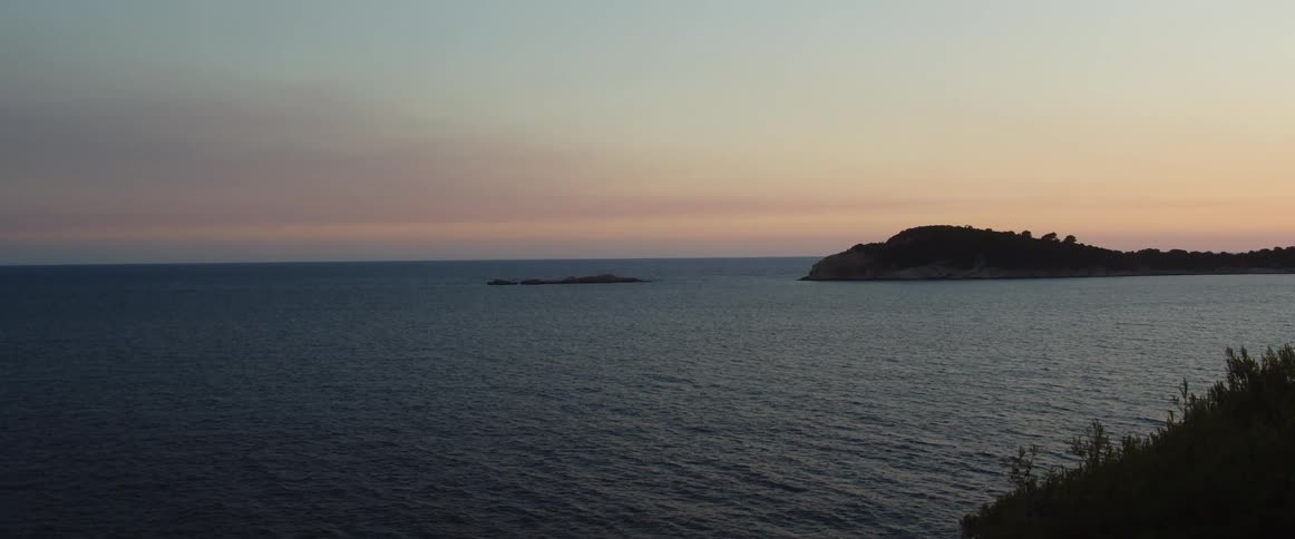 A coastal view of an ocean an island at sunset