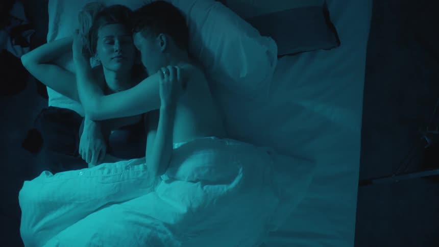 Couple cuddle while lying on bed in dark bedroom