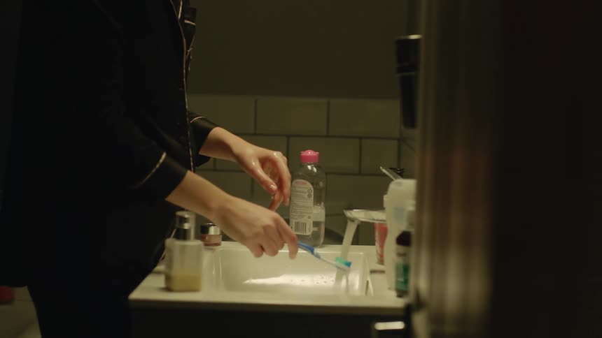 A woman brushing her teeth and getting ready for bed at a bathroom sink