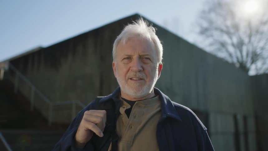 Man wearing a dark jacket is standing in front of a building