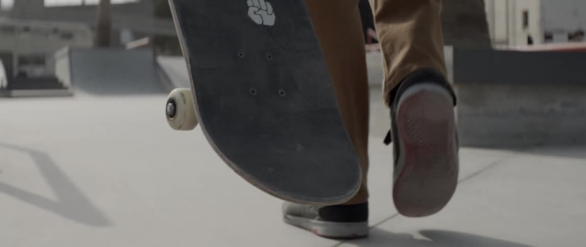 A man walks on a sidewalk with a skateboard in hand