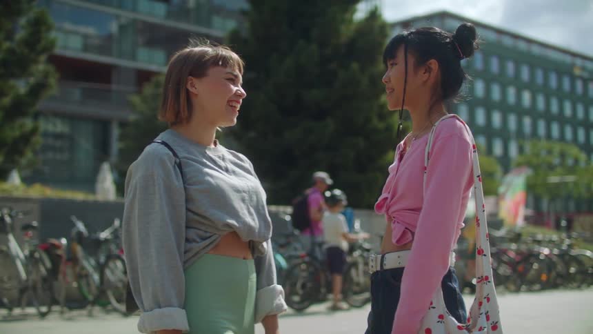 Female friend greet each other with a fist bump and hug standing and talking with parked bicycles in background