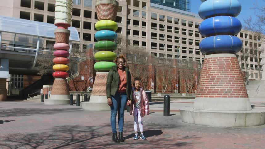 A woman and child are standing outside a building holding hands