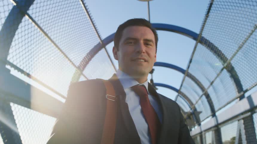 A man with a bag a suit and a tie in a overpass with the sky and clouds in the background