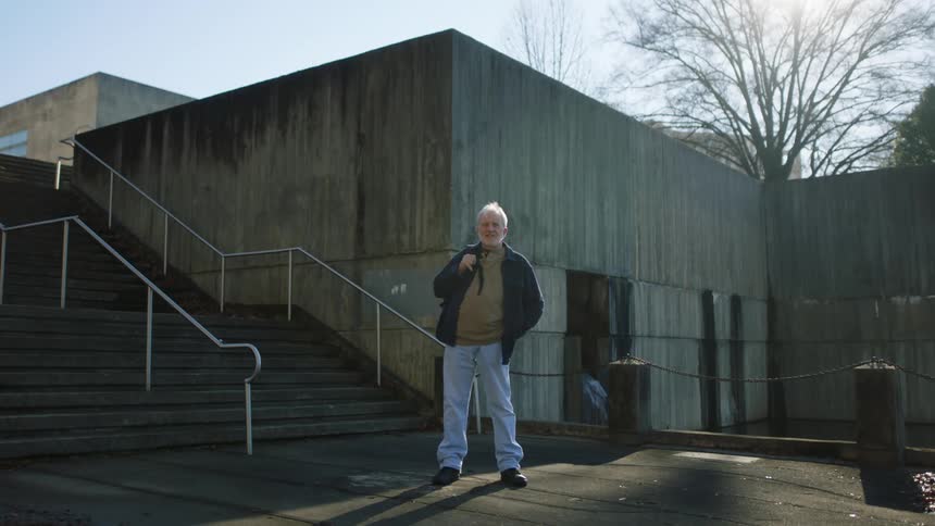 A man poses at the bottom of a staircase next to a concrete building