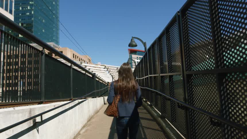 A female pedestrian wearing a face mask while walking across a city bridge