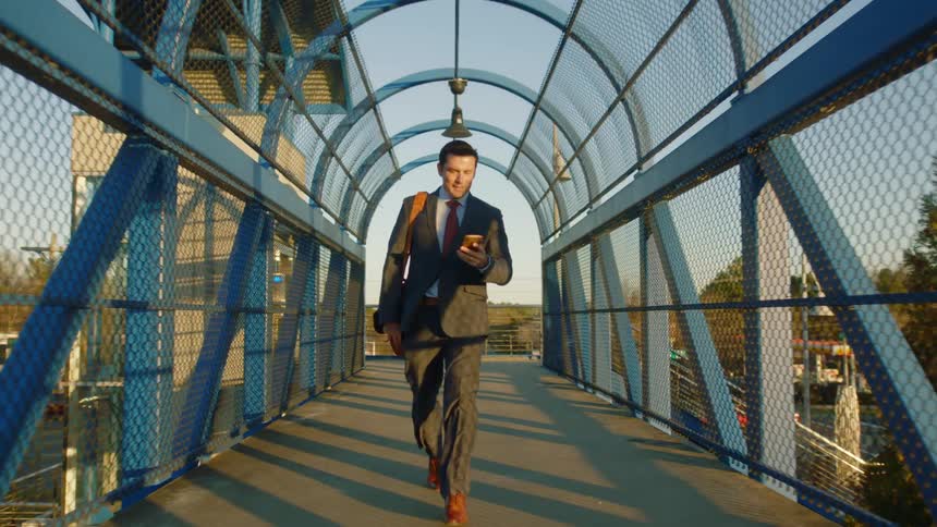 A businessman in a suit making a phone call while walking across an urban pedestrian bridge