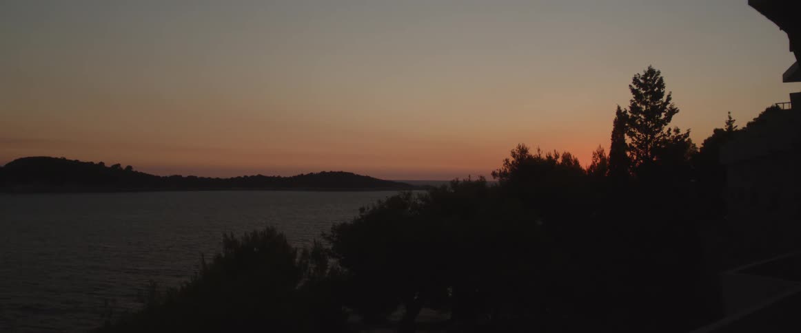 Silhouette of trees in the foreground with a lake the sky and clouds in the background