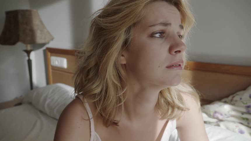Woman sits on a bed and looks concerned