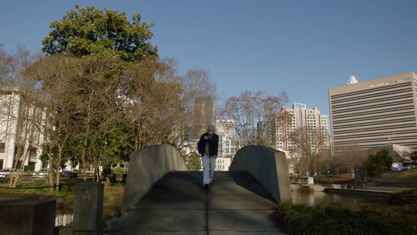 A man is bundled up walking over a footbridge in a city