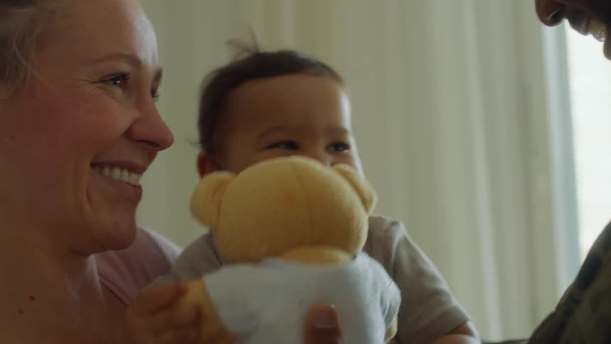 A mother and father hugging and smiling while interacting with their baby
