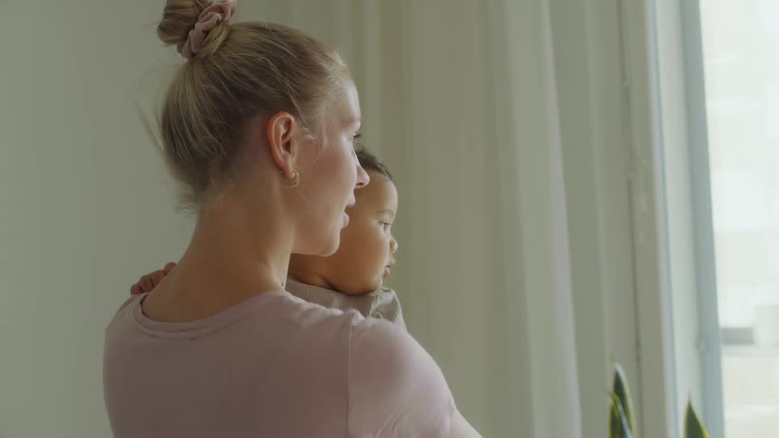 A woman holds and kisses a baby while pointing things out to him with a her finger