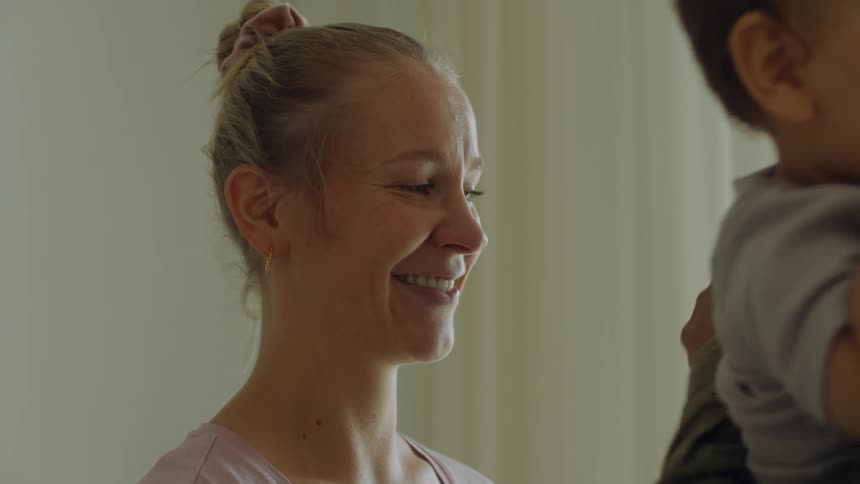 A mother smiling while watching her husband play with their baby