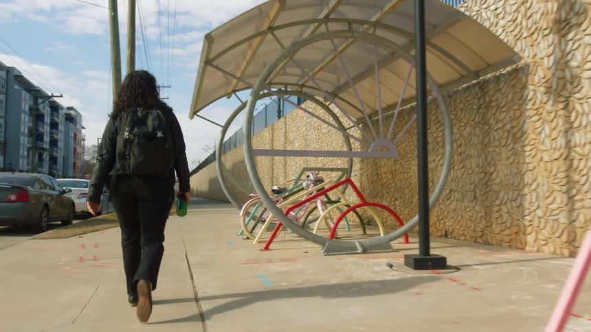 A woman walks along a sidewalk to a bike stand where she retrieves her bike