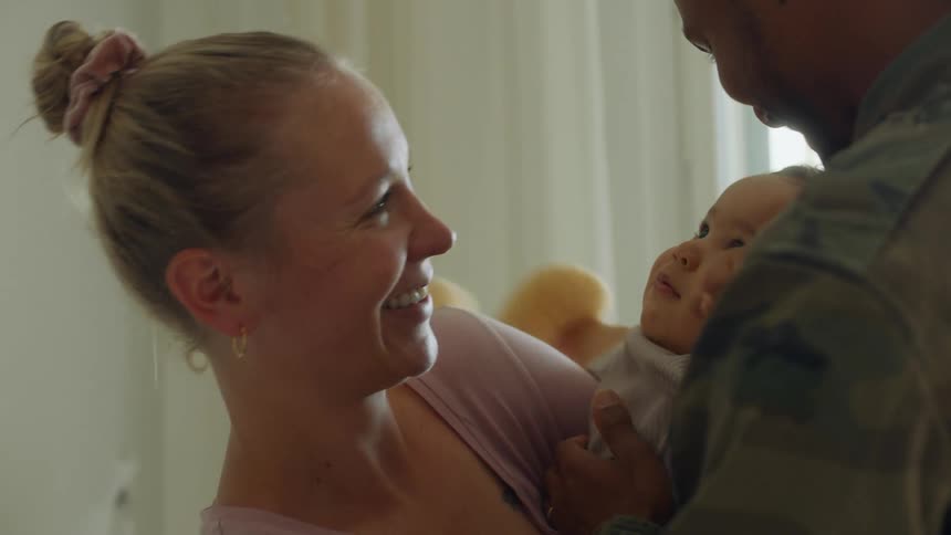 A mom and dad are holding their baby and kiss and smile