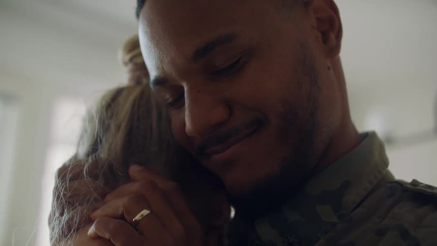 A man in camo smiles lovingly at his wife and hugs her caressing the nape of her neck