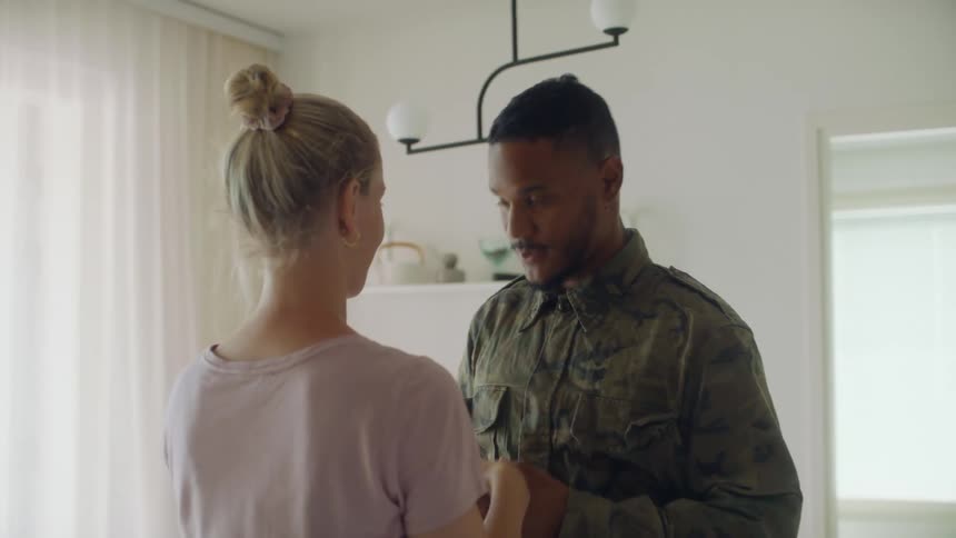 A male servicemember hugging and kissing his wife indoors