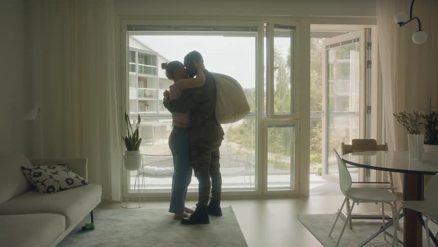 A soldier embraces and kisses his wife who is holding a baby