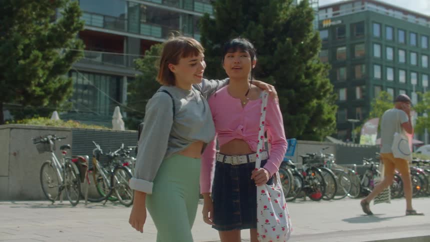 Two girls greet and hug then walk down the street