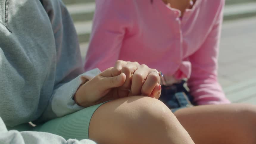 Two women are sitting on stairs and one grabs the hand of the other