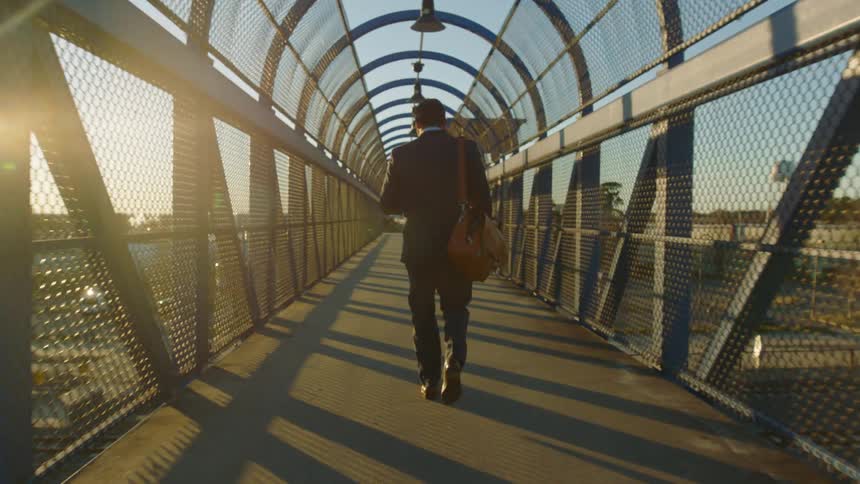 A man in a full suit walks on a pedestrian bridge downtown