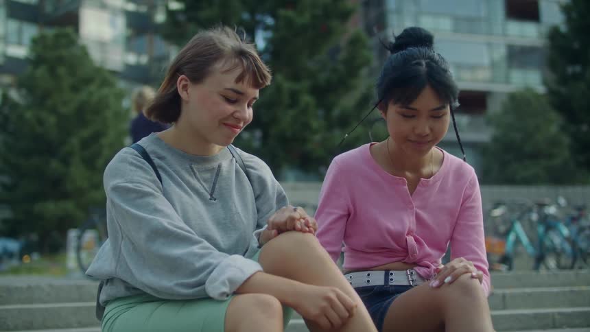 Two girls hold hands while sitting on the steps outside