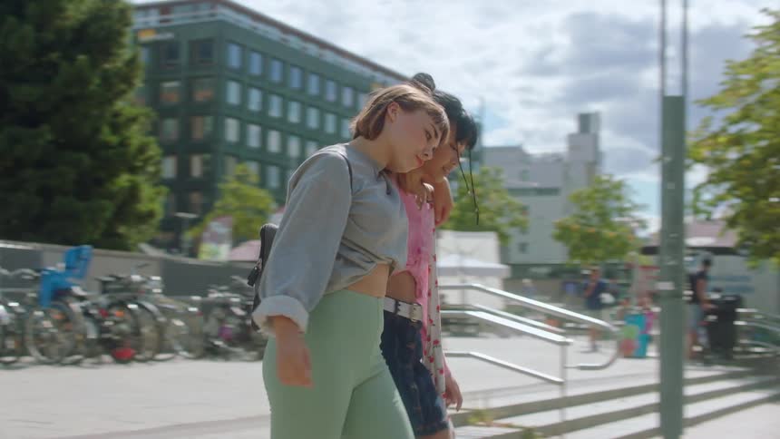 Two girls greet each other with a fist bump and a hug before walking down the sidewalk together
