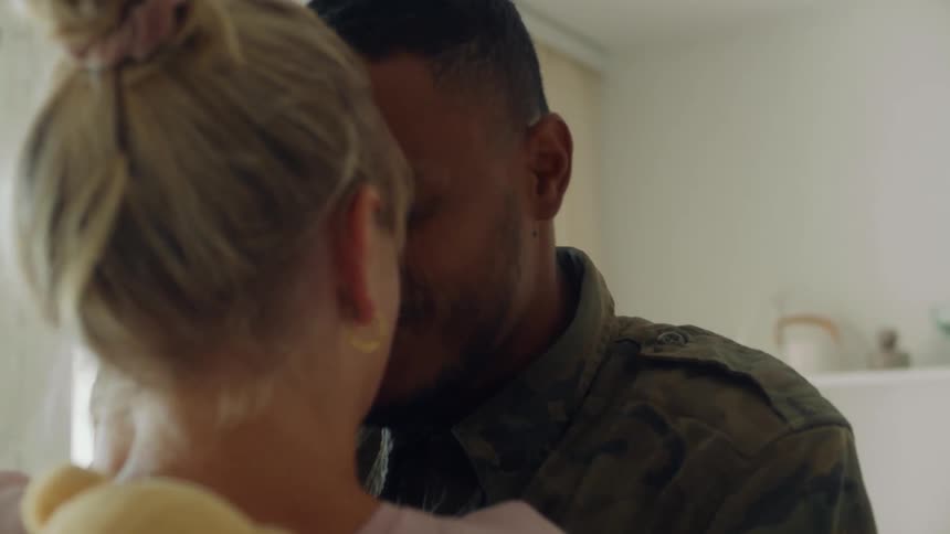 A man and a woman hugging and kissing while holding a baby in a room with a wall and a doorway in the background