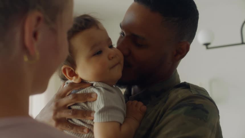 A husband and wife kissing while holding their baby