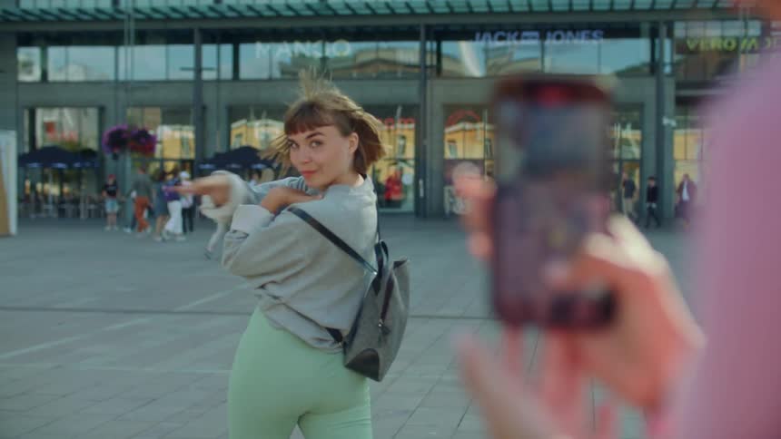 A teen girl being filmed on a smartphone while dancing on a busy city sidewalk