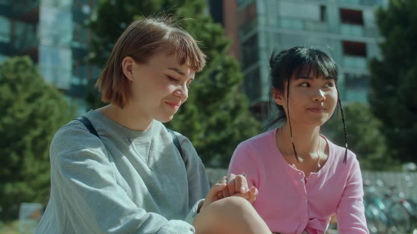 A girl tentatively reaches over and holds a friends hand and they both smile