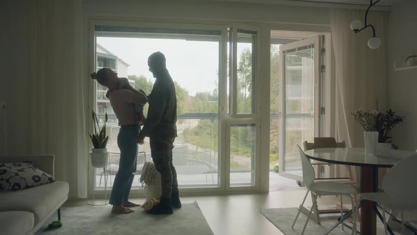 A man a woman and a child hugging in a room with a doorway a wall and a window in the background