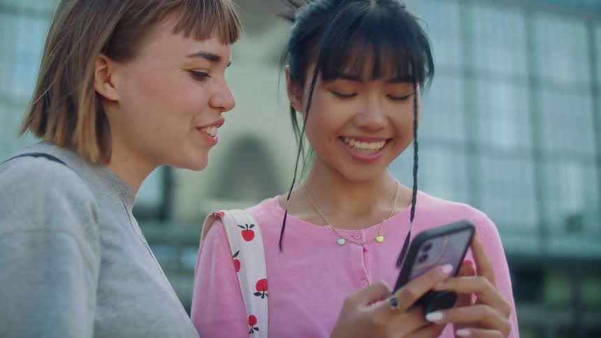 Two teen girls smiling and talking while looking at a smartphone