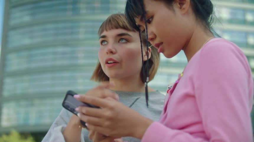 Two teenage girls talking while looking at a smartphone outdoors