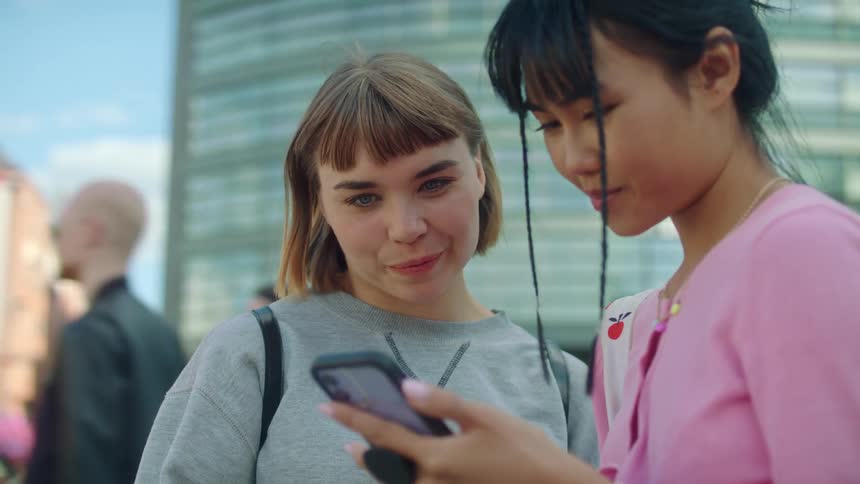 Two young women are looking at a cellphone and smiling