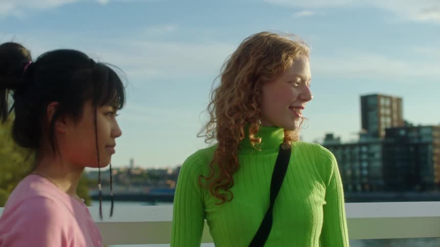Three girls are talking and give each other a group hug with a city and lake in the distance