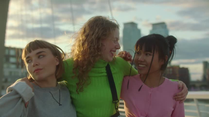Three women walk together hugging and laughing