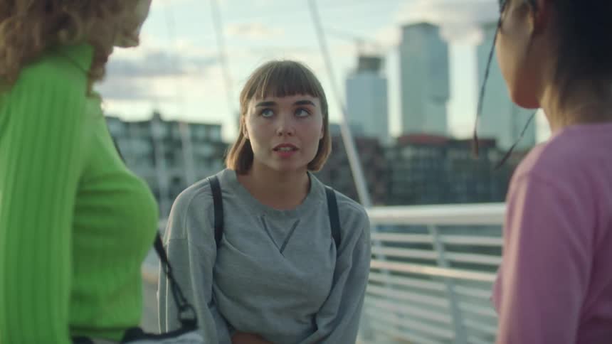 Three teenage girls looking sad while hugging and saying goodbye on a pedestrian bridge