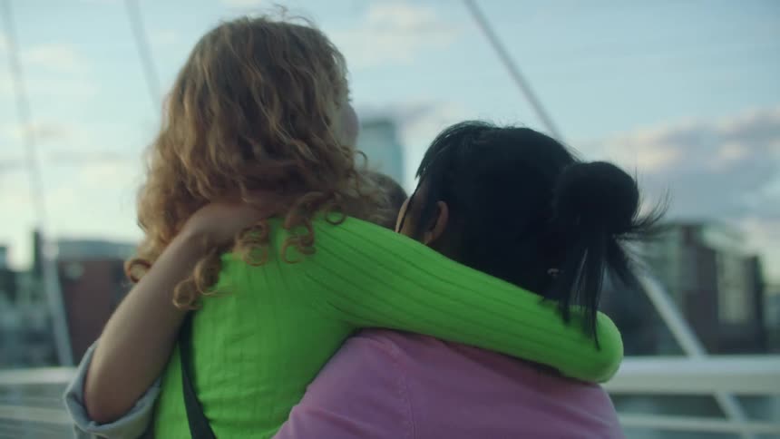 Three girl friends hug each other and say good bye on a pedestrian bridge as one walks away