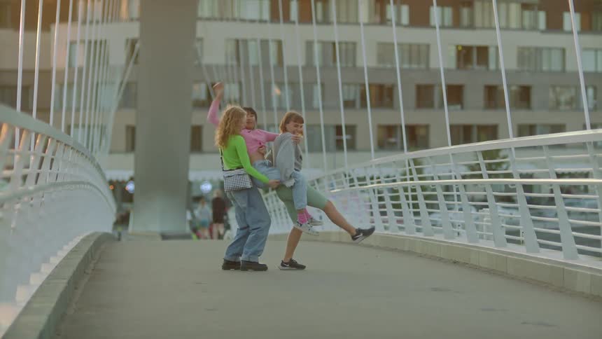 Three girl friends laugh as they walk across a pedestrian bridge carrying each other