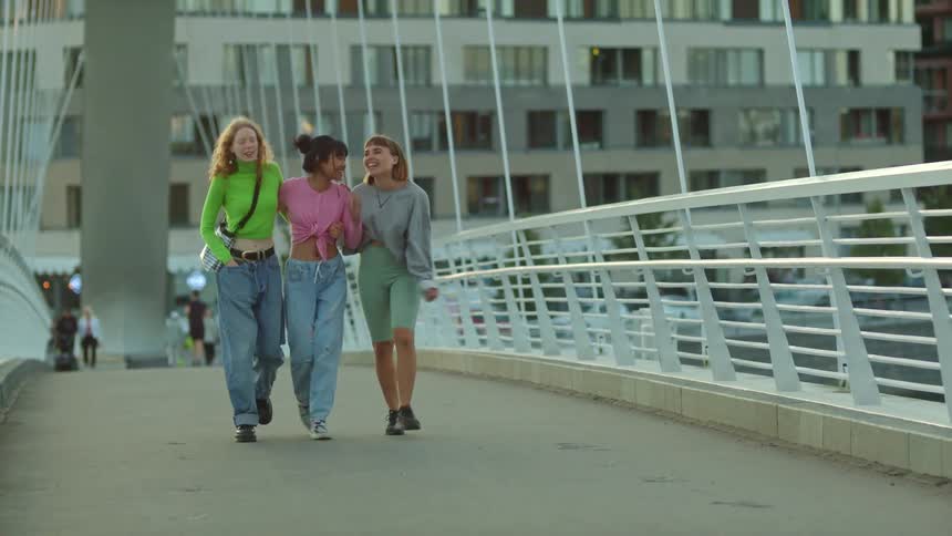A group of young women walk across a bridge with their arms around one another